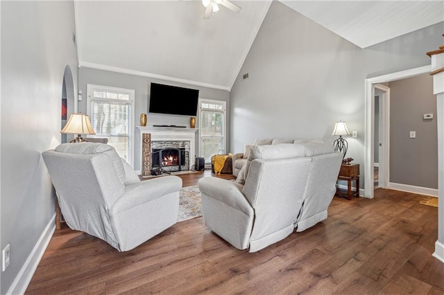living area featuring a ceiling fan, baseboards, a lit fireplace, dark wood-type flooring, and high vaulted ceiling