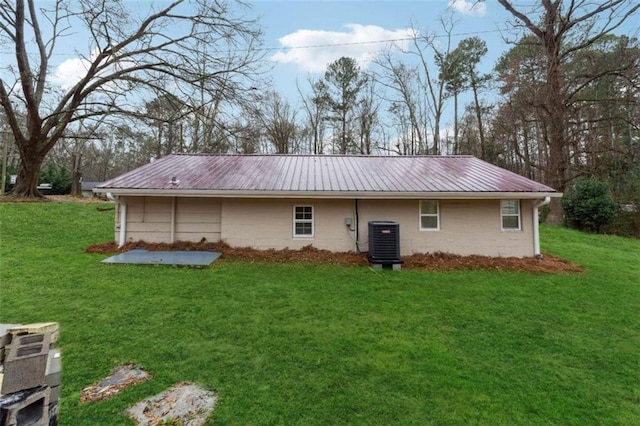 rear view of property featuring central air condition unit, metal roof, a yard, and concrete block siding