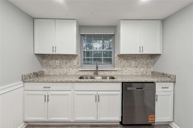 kitchen with a sink, white cabinets, wainscoting, stainless steel dishwasher, and tasteful backsplash