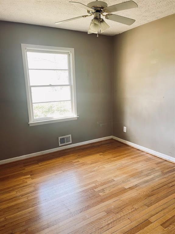 unfurnished room featuring visible vents, baseboards, light wood-type flooring, a textured ceiling, and a ceiling fan