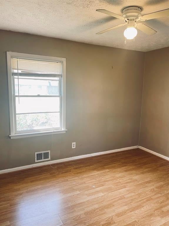 empty room featuring light wood finished floors, visible vents, a textured ceiling, and baseboards
