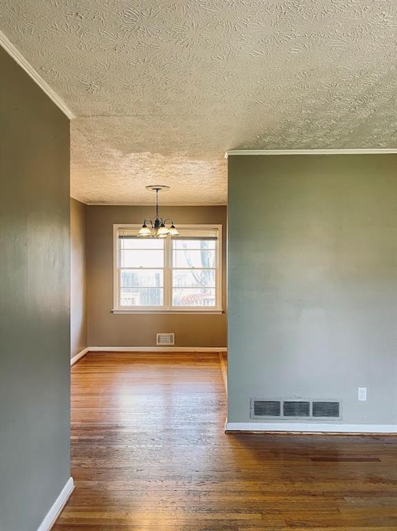 unfurnished room with a chandelier, visible vents, and wood finished floors