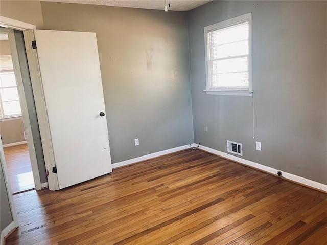 unfurnished room featuring visible vents, a healthy amount of sunlight, baseboards, and wood-type flooring