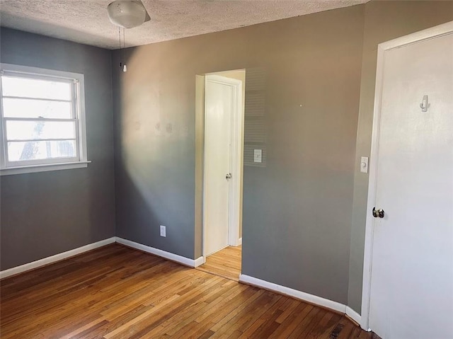 unfurnished room featuring hardwood / wood-style flooring, baseboards, and a textured ceiling
