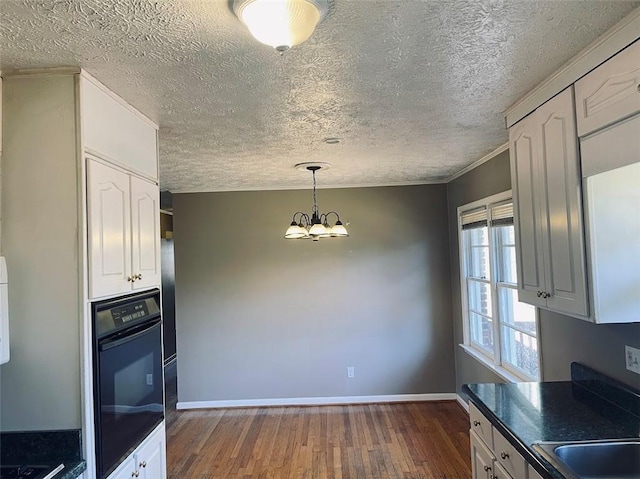 kitchen with dark wood finished floors, white cabinets, dark countertops, black oven, and a notable chandelier