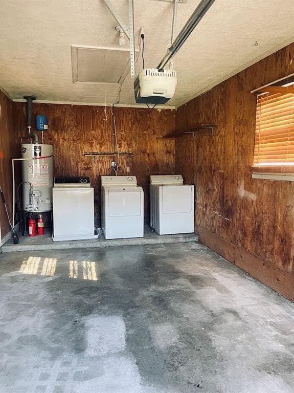 garage featuring a garage door opener, water heater, wood walls, and washing machine and clothes dryer