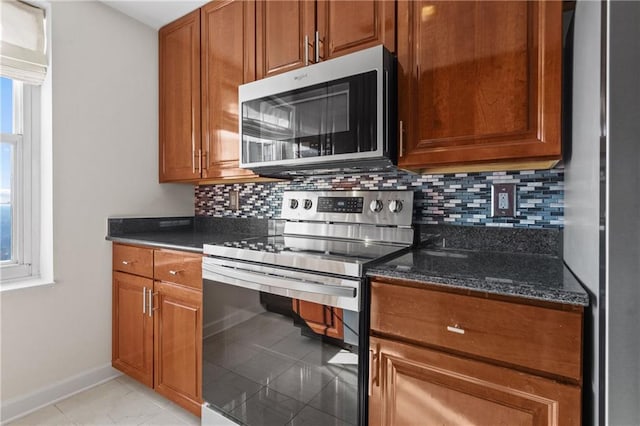 kitchen with brown cabinetry, baseboards, dark stone counters, stainless steel appliances, and tasteful backsplash