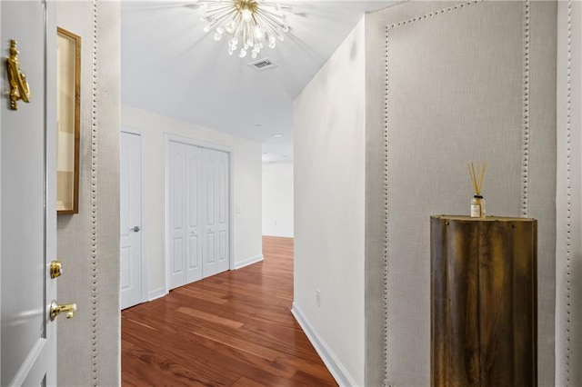 hallway with visible vents, baseboards, wood finished floors, and a chandelier