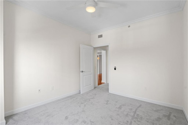 carpeted empty room featuring crown molding, visible vents, baseboards, and ceiling fan