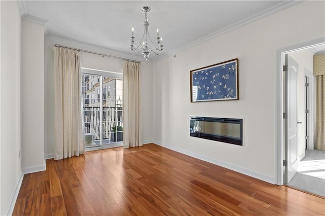 unfurnished dining area featuring wood finished floors, baseboards, an inviting chandelier, ornamental molding, and a glass covered fireplace