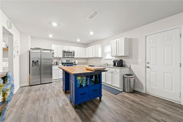 kitchen with blue cabinetry, white cabinetry, a center island, butcher block countertops, and appliances with stainless steel finishes