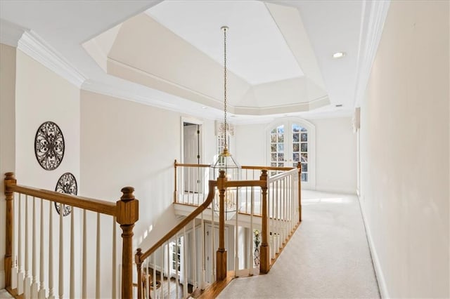 corridor with a tray ceiling, crown molding, light colored carpet, and a notable chandelier