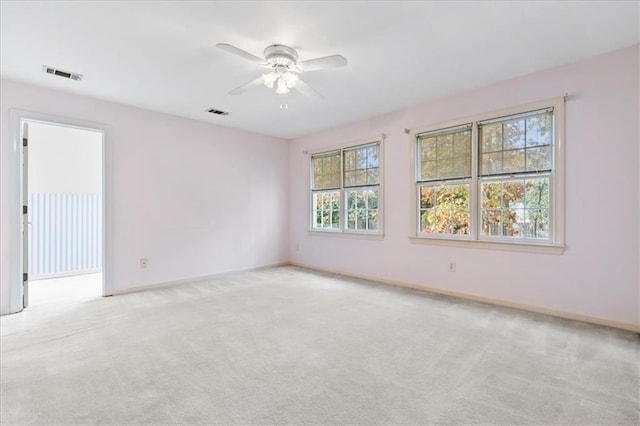 empty room with a wealth of natural light, light colored carpet, and ceiling fan