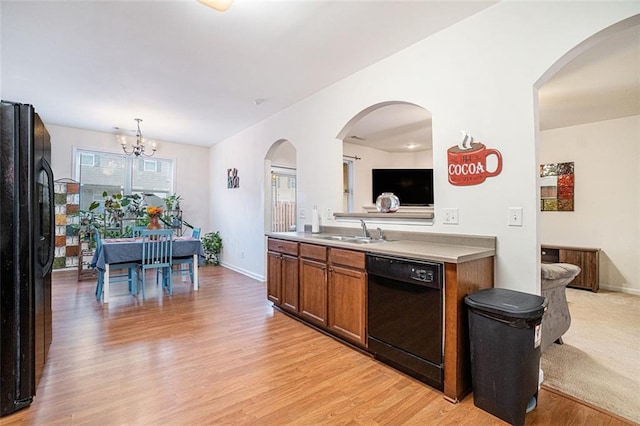 kitchen featuring sink, a chandelier, hanging light fixtures, light wood-type flooring, and black appliances