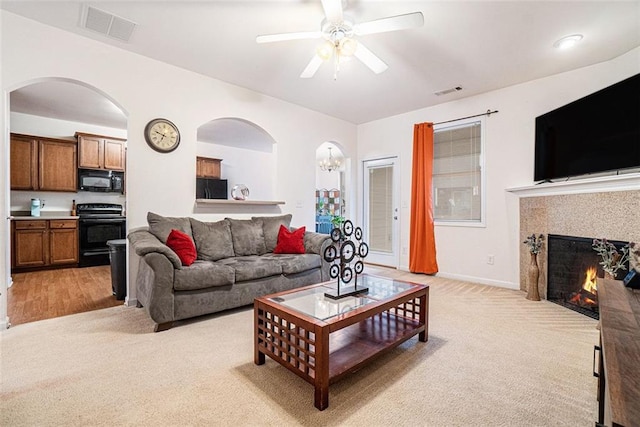 carpeted living room featuring ceiling fan with notable chandelier and a fireplace