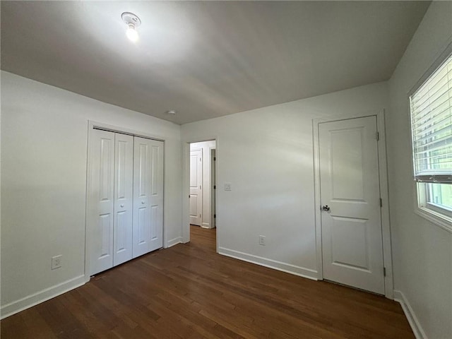 unfurnished bedroom featuring a closet, baseboards, and dark wood-style flooring