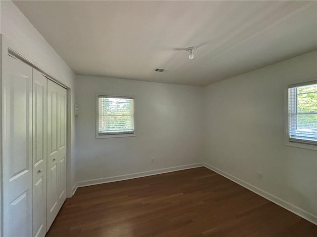 unfurnished bedroom with visible vents, baseboards, a closet, and dark wood-style floors