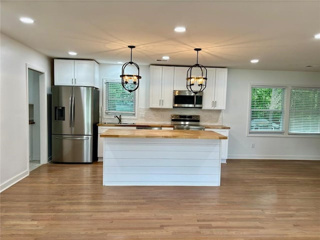 kitchen featuring wood finished floors, stainless steel appliances, decorative backsplash, white cabinets, and butcher block counters