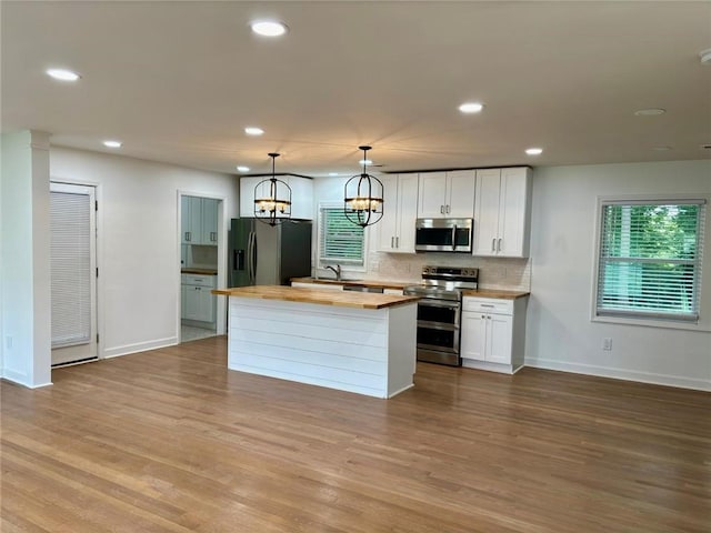 kitchen with wood counters, a kitchen island, tasteful backsplash, wood finished floors, and stainless steel appliances