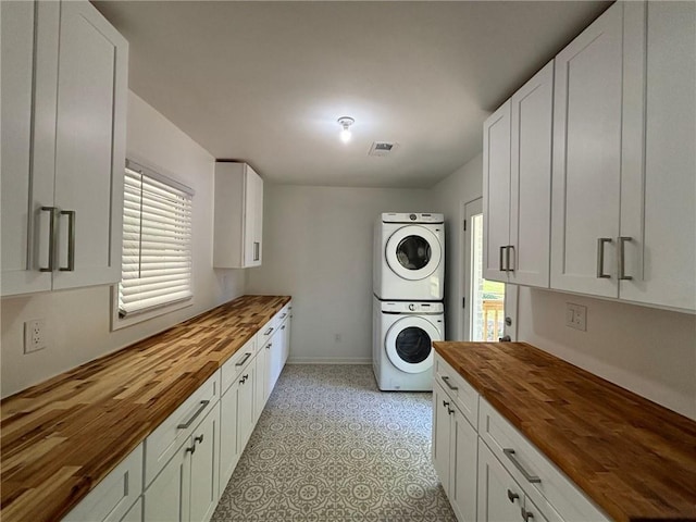 clothes washing area with cabinet space, visible vents, stacked washer / drying machine, and baseboards