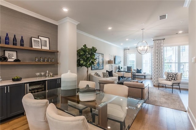 dining room featuring visible vents, light wood-style flooring, an inviting chandelier, ornamental molding, and a bar