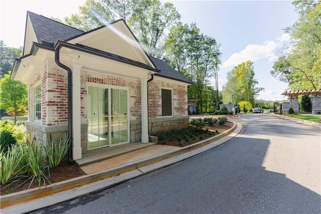 view of property exterior with stone siding, a shingled roof, and brick siding