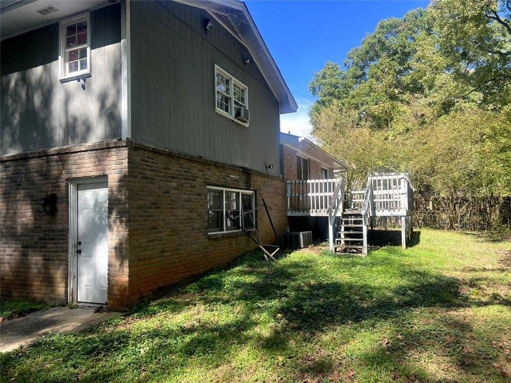 view of property exterior featuring a wooden deck, central AC, a lawn, and brick siding