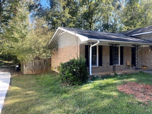 view of side of home with a yard, fence, a porch, and brick siding