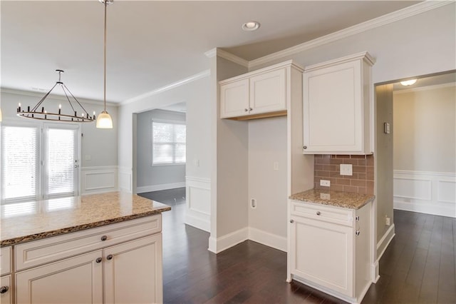 kitchen with light stone counters, dark wood-style flooring, a notable chandelier, and wainscoting