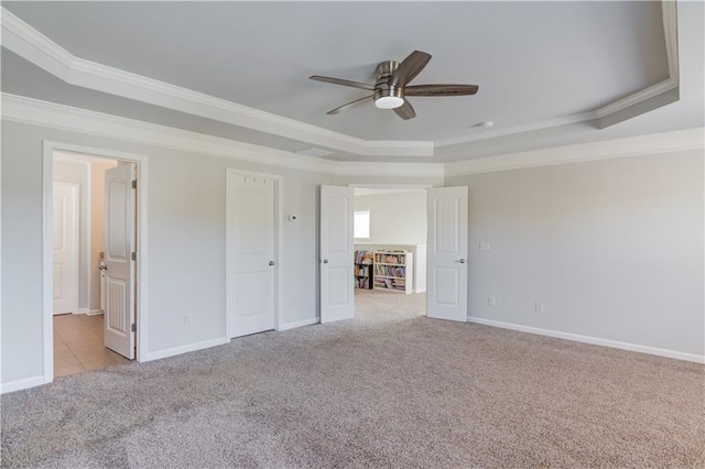 unfurnished bedroom featuring crown molding, a tray ceiling, baseboards, and light colored carpet