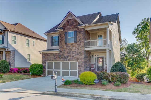 craftsman inspired home with an attached garage, stone siding, a balcony, driveway, and roof with shingles
