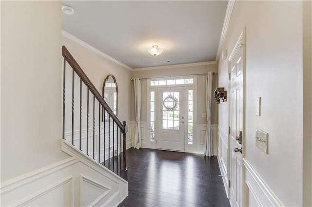 foyer entrance with stairway, crown molding, a wainscoted wall, dark wood finished floors, and a decorative wall