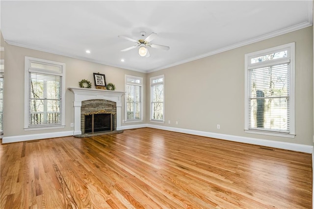 unfurnished living room with ceiling fan, a stone fireplace, ornamental molding, and a wealth of natural light