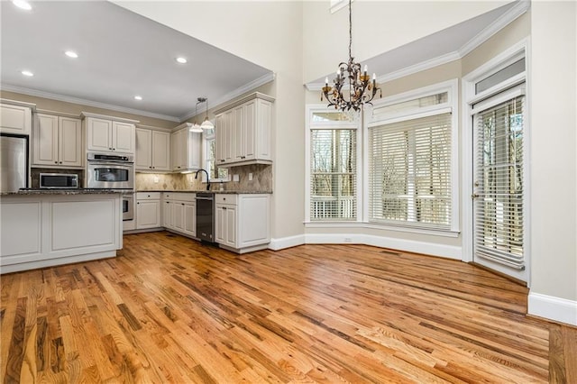 kitchen featuring tasteful backsplash, stainless steel appliances, pendant lighting, light hardwood / wood-style flooring, and a notable chandelier