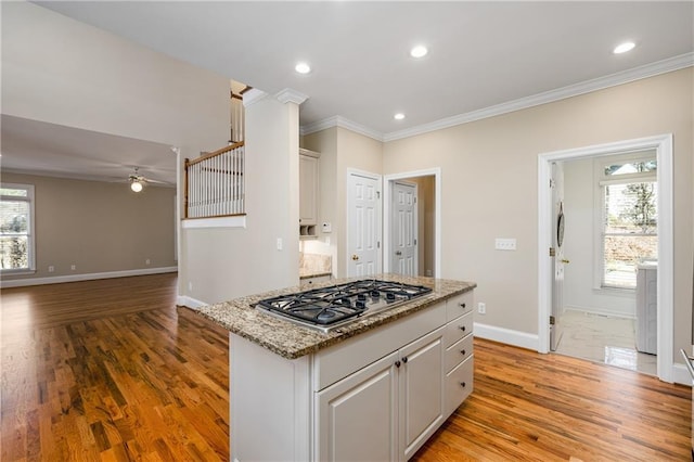 kitchen with ceiling fan, light stone counters, light hardwood / wood-style floors, stainless steel gas stovetop, and ornamental molding