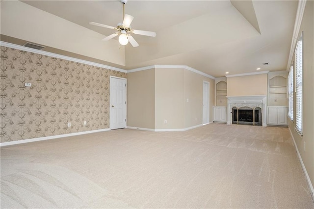 unfurnished living room featuring built in shelves, light colored carpet, ceiling fan, crown molding, and a premium fireplace