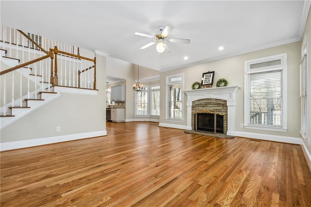 unfurnished living room with ceiling fan with notable chandelier, wood-type flooring, a fireplace, and ornamental molding