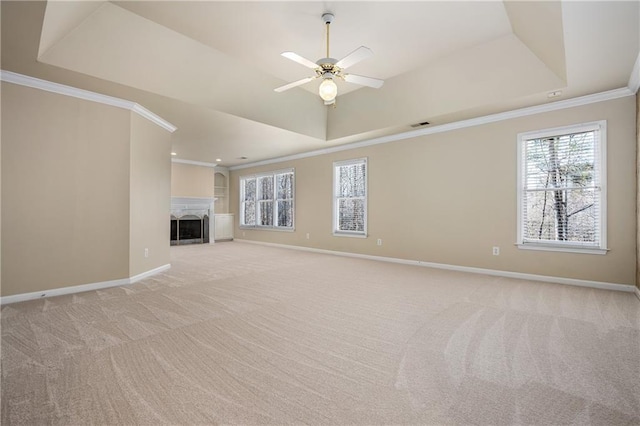 unfurnished living room with a raised ceiling, crown molding, ceiling fan, and light colored carpet