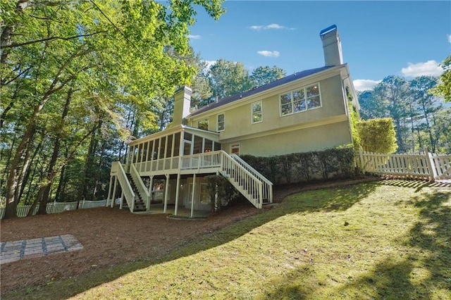 rear view of house featuring a sunroom, a wooden deck, and a lawn