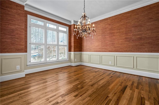 unfurnished dining area featuring hardwood / wood-style flooring, ornamental molding, and an inviting chandelier