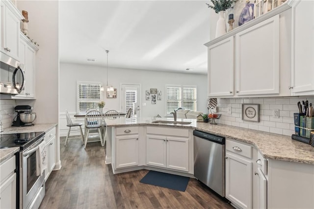 kitchen featuring a sink, dark wood-style floors, white cabinetry, stainless steel appliances, and a peninsula