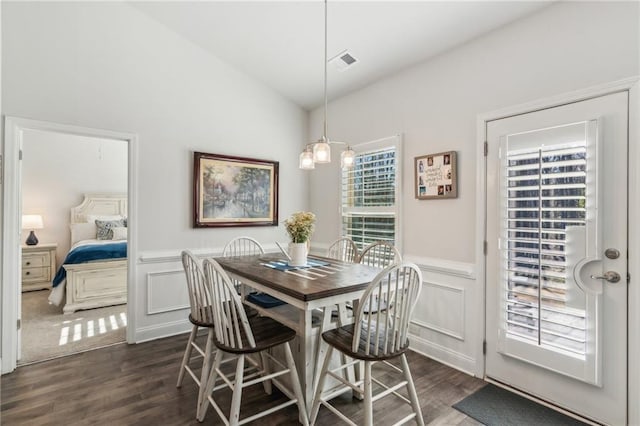 dining area featuring visible vents, lofted ceiling, dark wood-style floors, and a wainscoted wall