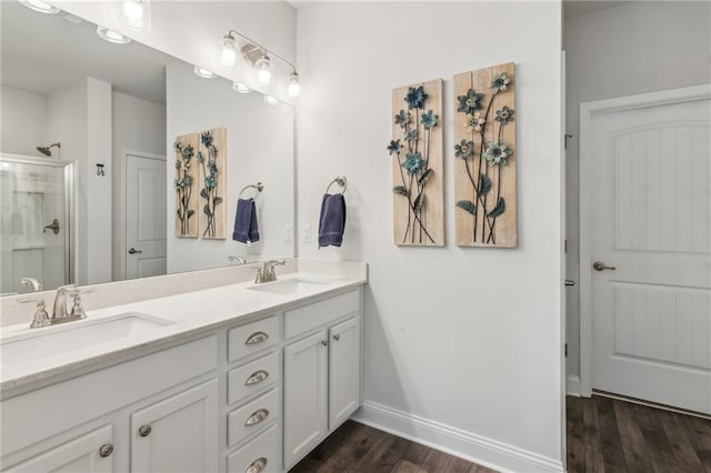 bathroom featuring double vanity, a shower, wood finished floors, and a sink