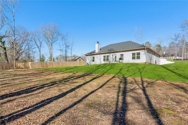 back of property featuring fence, a lawn, and a chimney