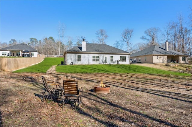 rear view of property with a chimney, a lawn, and an outdoor fire pit