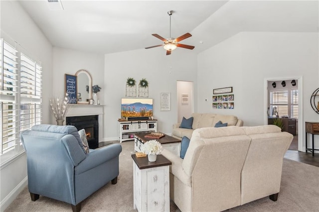 living room with a ceiling fan, baseboards, visible vents, vaulted ceiling, and a glass covered fireplace