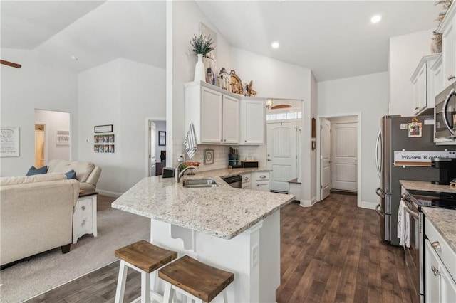 kitchen with a kitchen bar, appliances with stainless steel finishes, a peninsula, white cabinets, and a sink