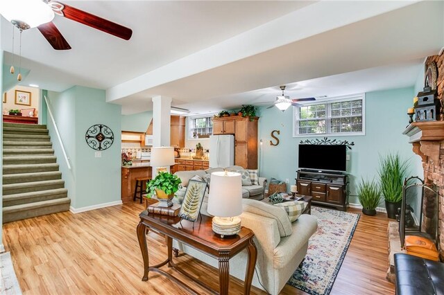 living room featuring a fireplace, ceiling fan, and light wood-type flooring