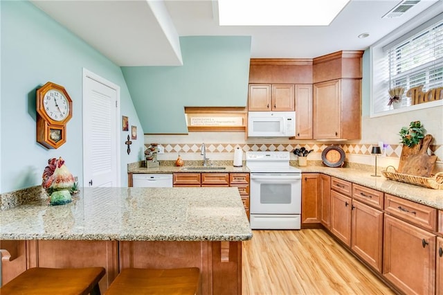 kitchen featuring white appliances, light stone countertops, sink, and a breakfast bar area