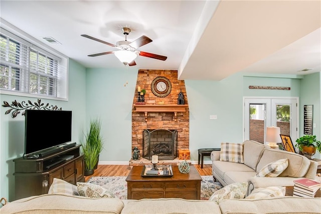 living room with a stone fireplace, wood-type flooring, french doors, and ceiling fan